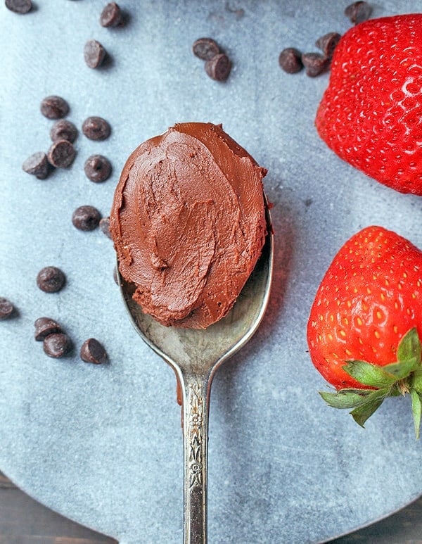 A spoon with chocolate frosting on it with mini chocolate chips and strawberries on each side. 