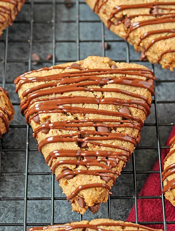 A chocolate chip scones with chocolate drizzle on a cooling rack.